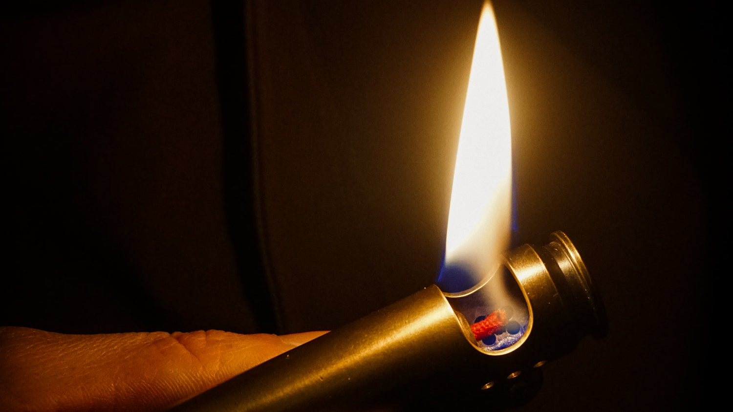 A real refillable wick lighter burning in an adult hand with its open mechanism visible