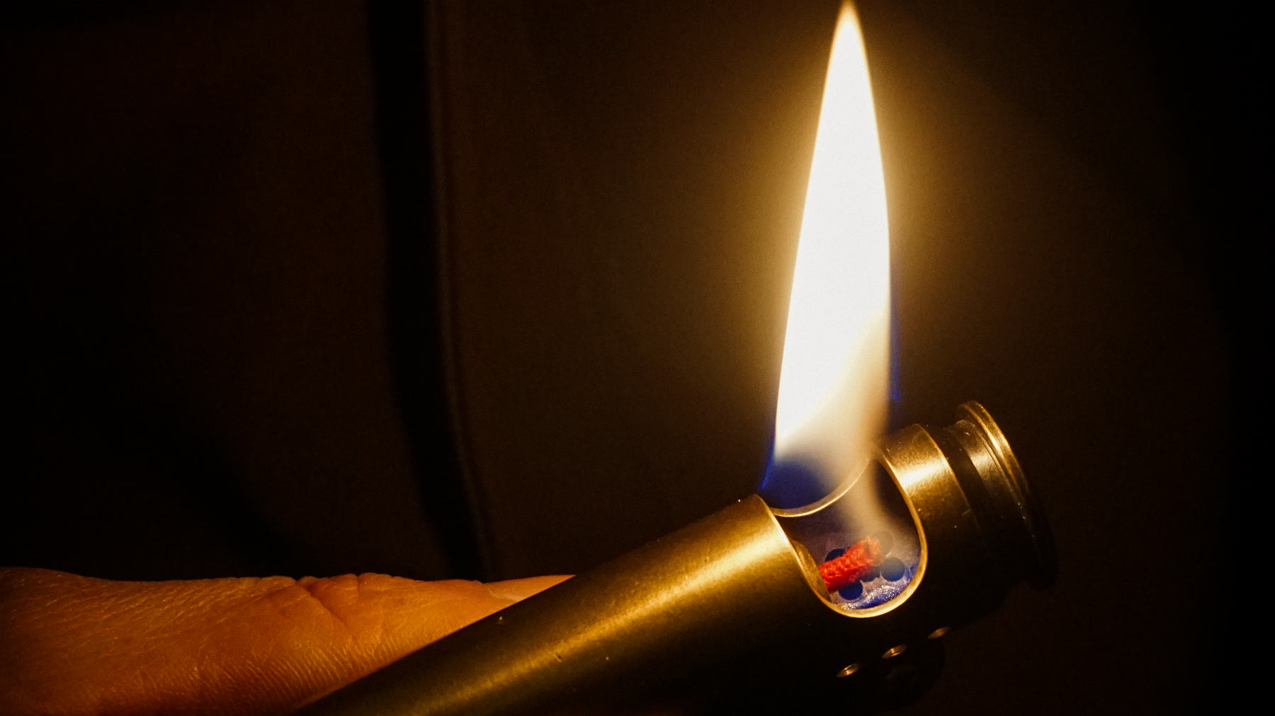 A real liquid-fuel wick lighter burning with its red wick and open mechanism visible
