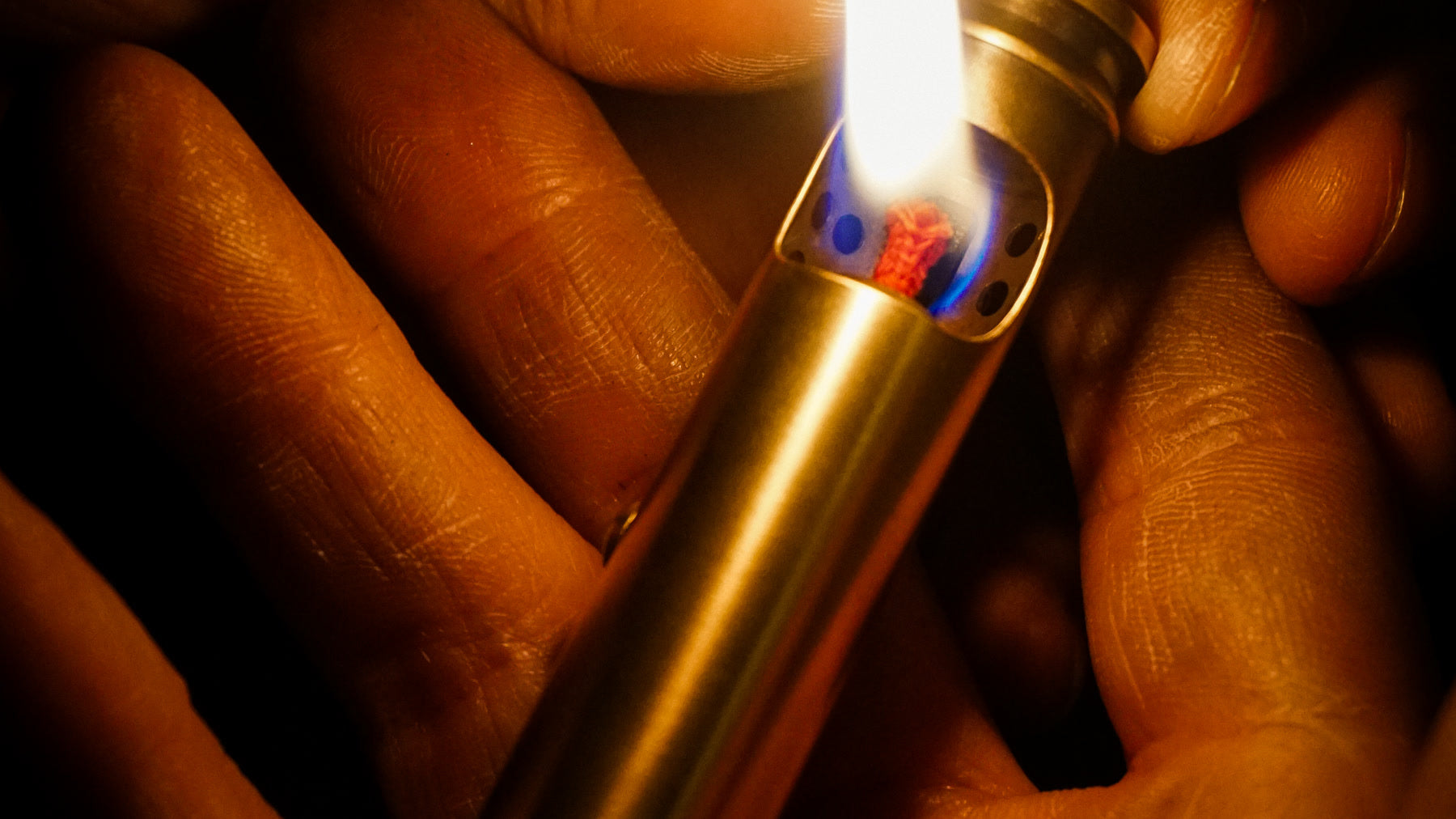 Small vintage-style brass lighter burning in adult hands