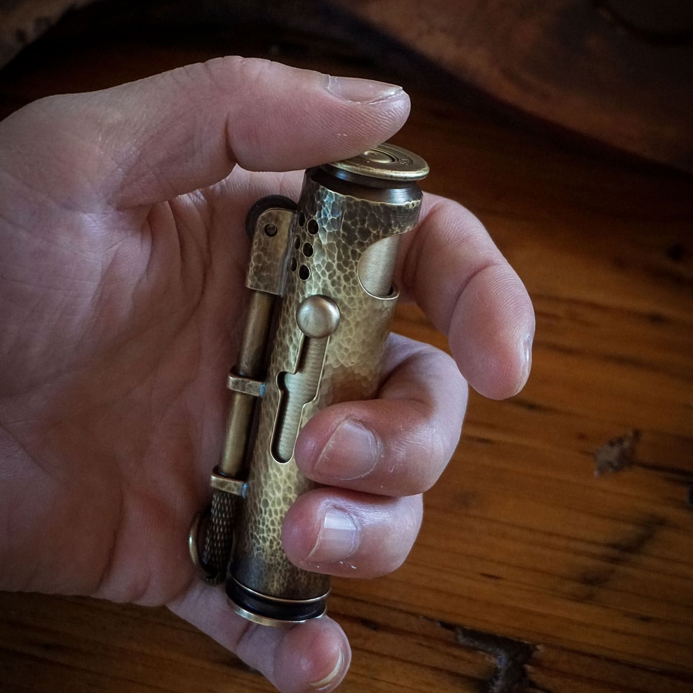 Hand holding a hammered WEDO brass shell lighter with bolt-action mechanism