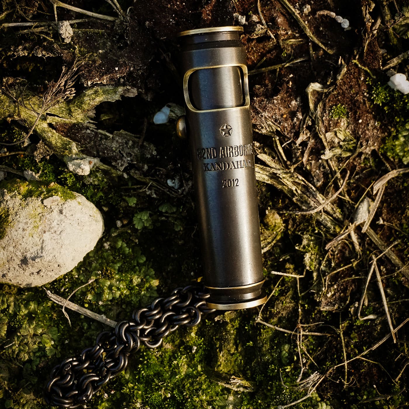 Military-inspired engraved brass lighter in dark finish displayed outdoors